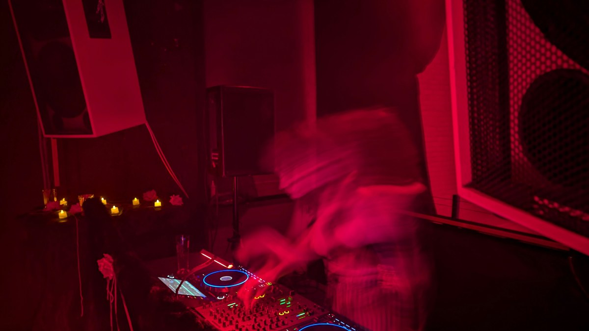 A DJ booth bathed in red light flanked by large PA speakers.