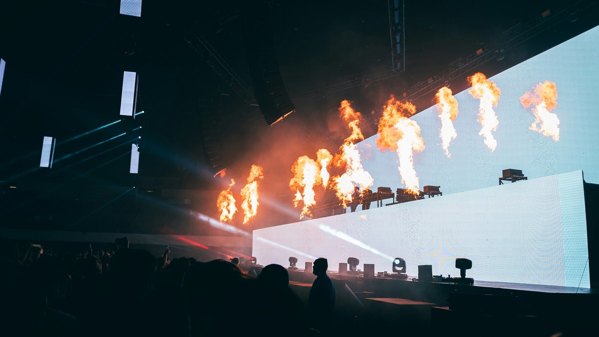 Flame jets erupting over a stage backed by a glowing LED wall.