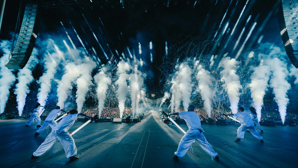 CO2 jets blasting over dancers on a festival stage with line array speakers overhead.
