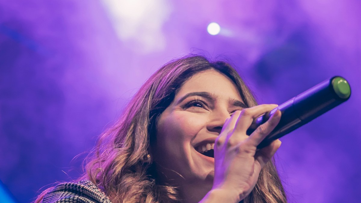 A singer holding a wireless microphone under purple stage light.