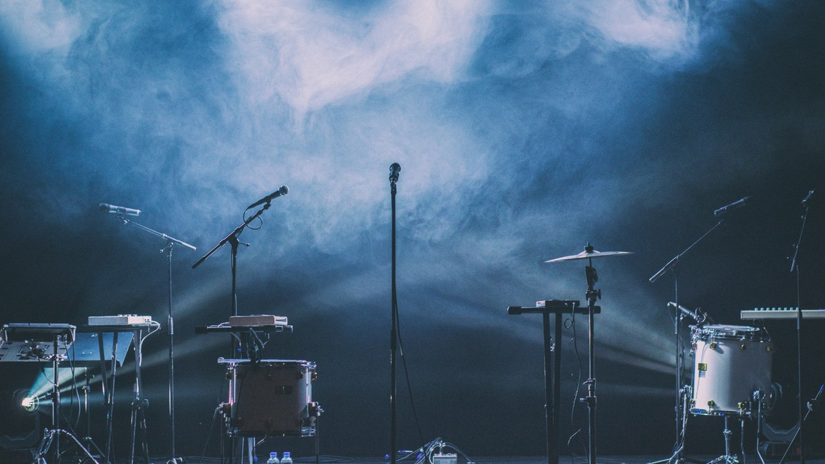 An empty stage set with microphones, drums and keyboards under blue haze.