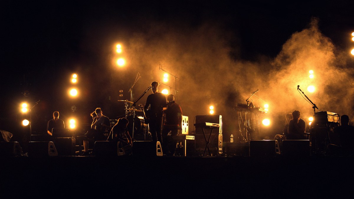 A band on stage silhouetted against warm amber stage lights and haze.