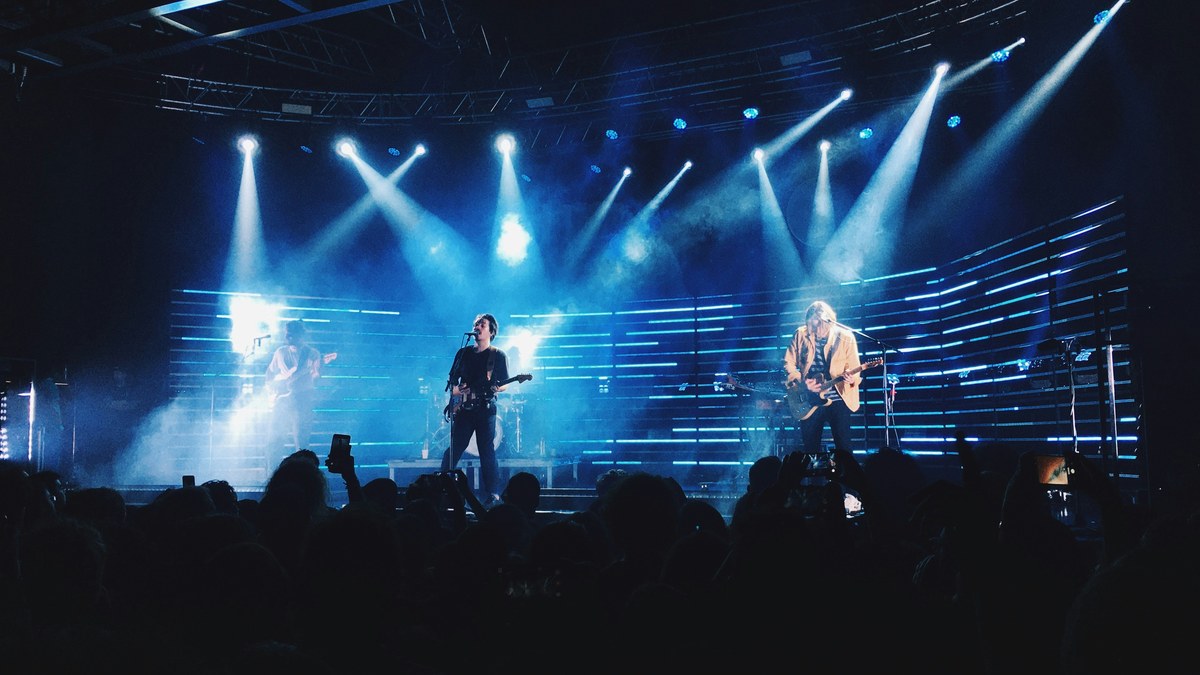 A band on stage in front of a blue LED light wall with moving-head beams.