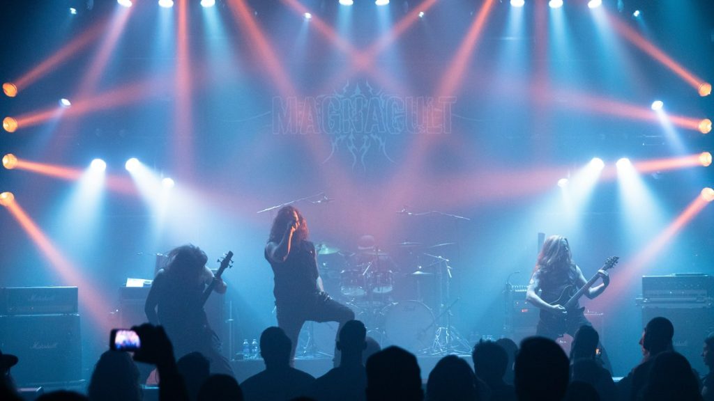 A metal band performing on stage under blue and orange lights