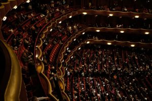 A packed Broadway theatre auditorium with tiered red seats and balconies