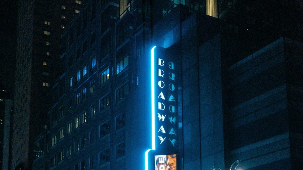 A vertical neon Broadway sign on a theatre at night in New York City