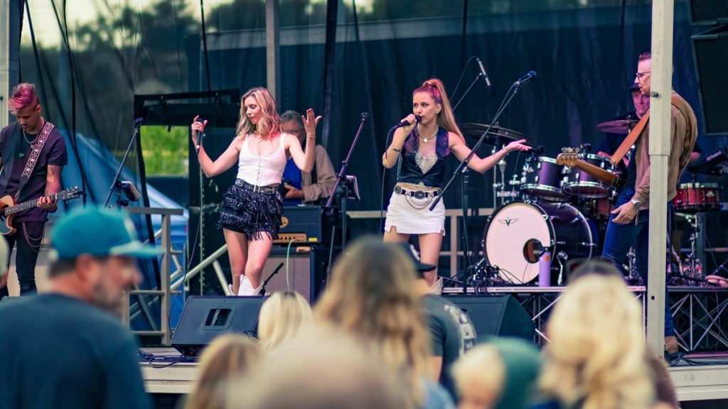 A band performing on an outdoor stage in daylight before a crowd