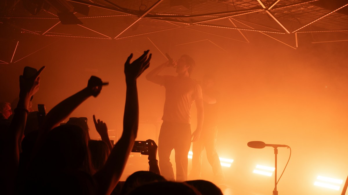 Crowd with hands raised at an orange-lit show