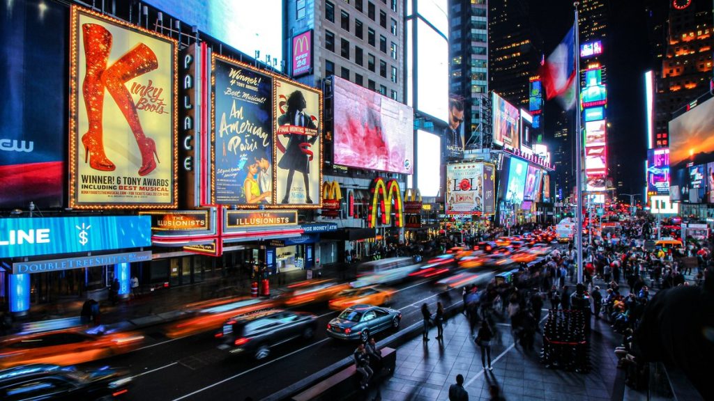 Times Square at night with Broadway theatre billboards and traffic light trails