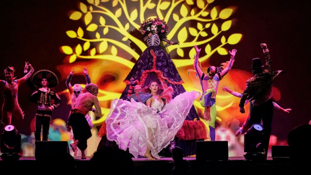 Dancers in colourful costumes performing on stage in front of a golden tree backdrop