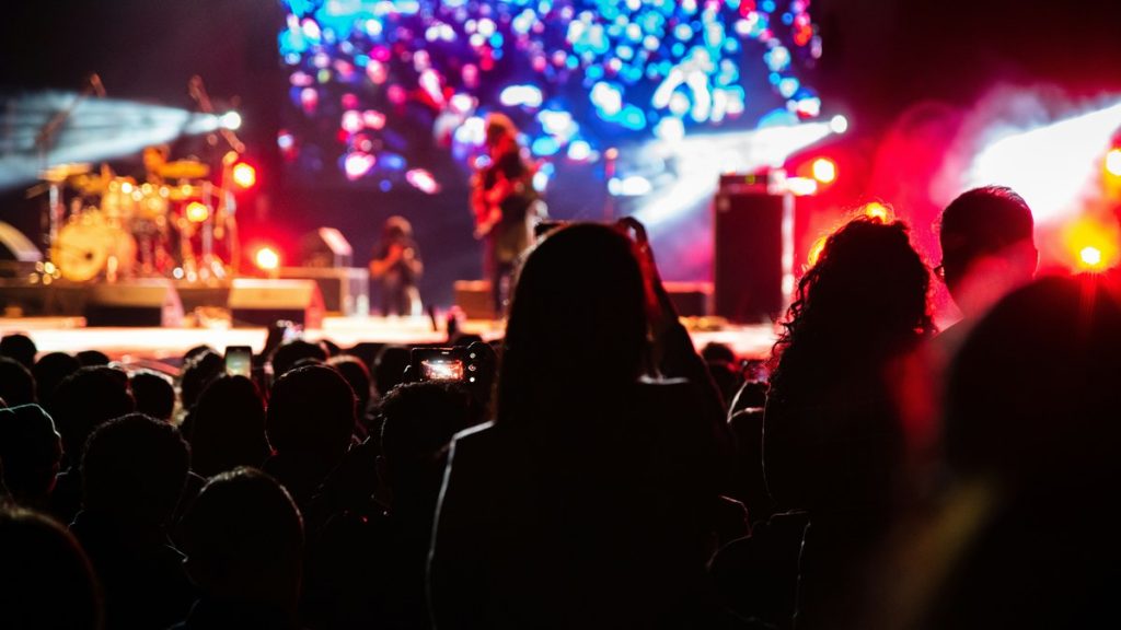A dense concert crowd silhouetted against red stage lights