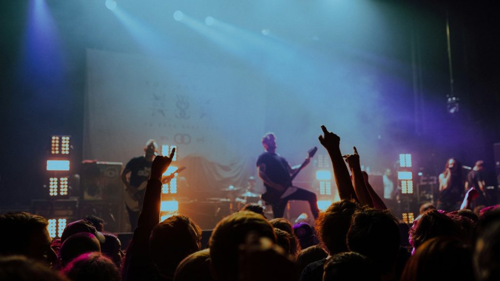 A rock band on stage as the crowd raises their hands