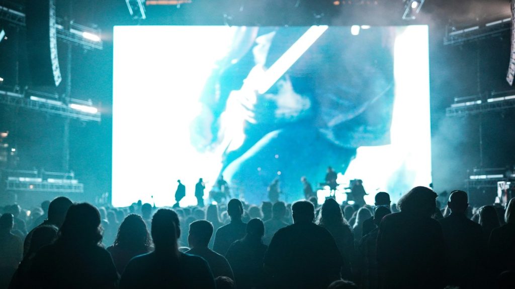 A large crowd gathered before a brightly lit arena stage