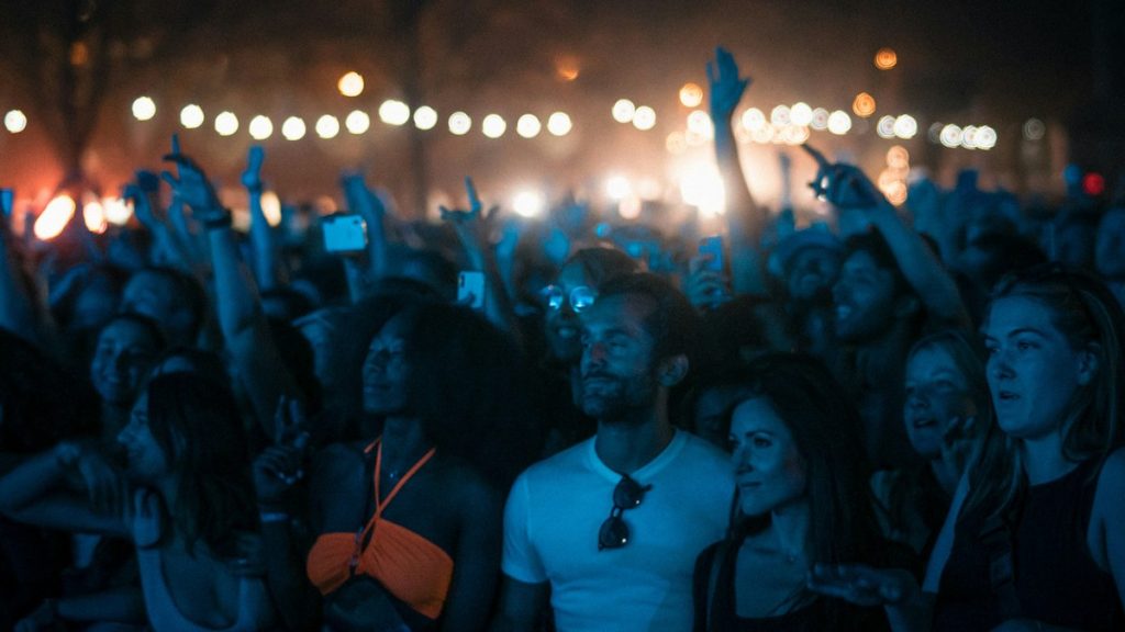 Concert crowd with hands raised under string lights at night