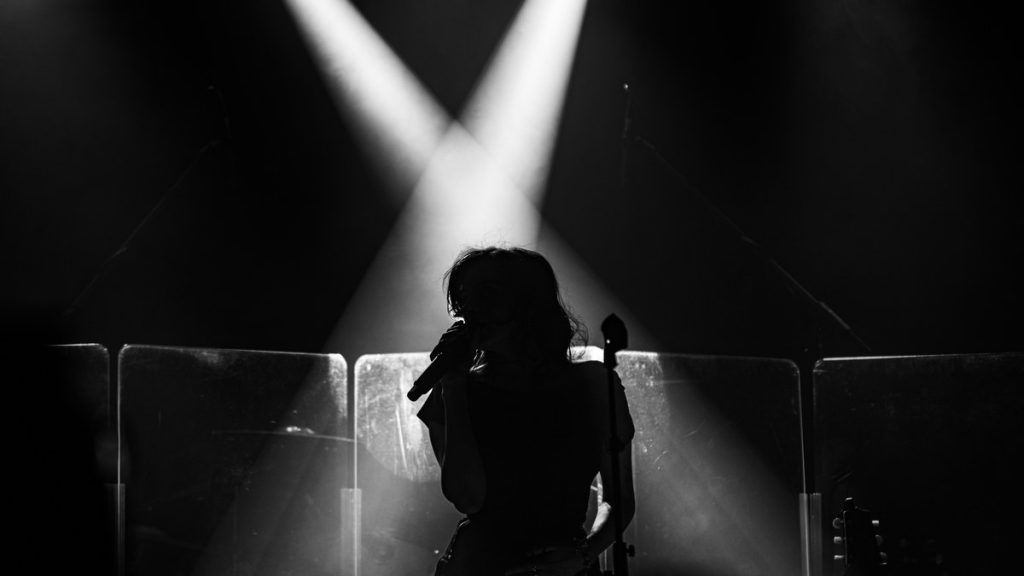 A singer silhouetted on stage under crossed spotlights
